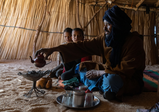 Tuareg man and children inside a reeed house preparing tea, North Africa, Tamanrasset, Algeria