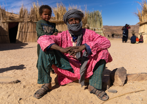 Tuareg man with his child sit in front of his reed house, North Africa, Tamanrasset, Algeria