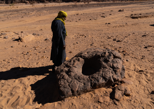 Tuareg man in front of a rock to store water in the desert, Tassili N'Ajjer National Park, Tadrart Rouge, Algeria