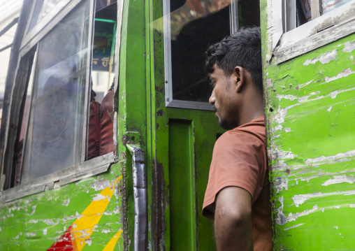 Bangladeshi man standing on the steps of a green scratched bus, Dhaka Division, Dhaka, Bangladesh