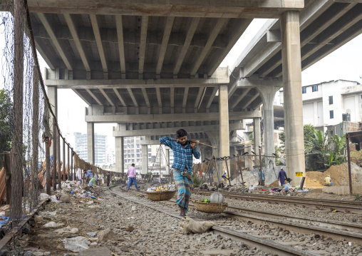 A bangladeshi man carries baskets along the rail track, Dhaka Division, Dhaka, Bangladesh