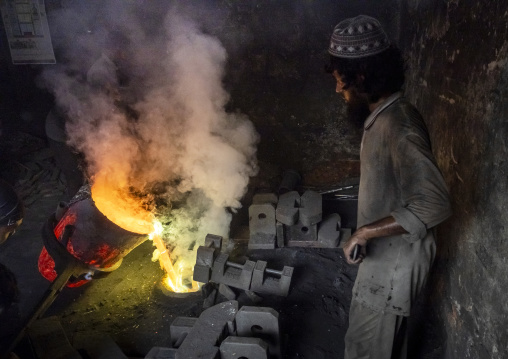 Bangladeshi man putting molten steel into a mold at Dhaka shipyard, Dhaka Division, Keraniganj, Bangladesh