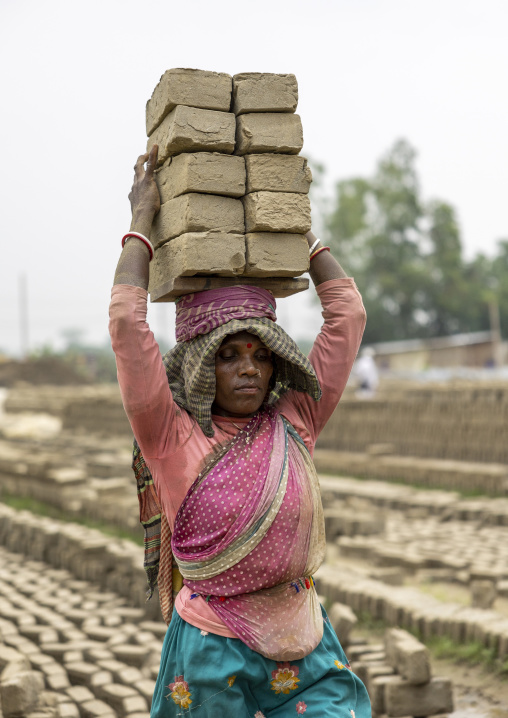 A bangladeshi woman carrying bricks on her head at a brick factory, Sylhet Division, Bahubal, Bangladesh