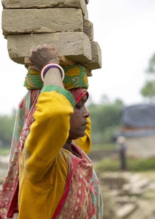 A bangladeshi woman carrying bricks on her head at a brick factory, Sylhet Division, Bahubal, Bangladesh