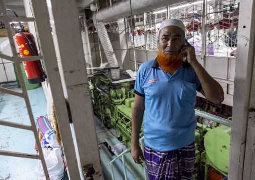 Bangladeshi man with red beard calling on phone in ferry engine room, Dhaka Division, Dhaka, Bangladesh