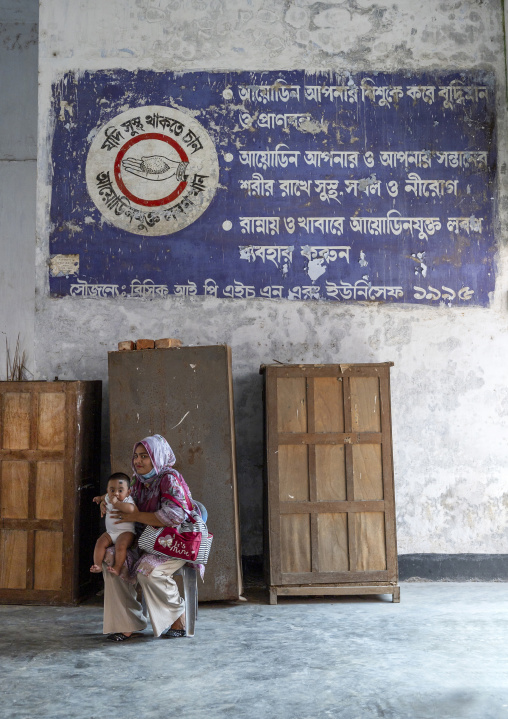 Woman with her baby under a mural about iodine, Khulna Division, Jessore, Bangladesh