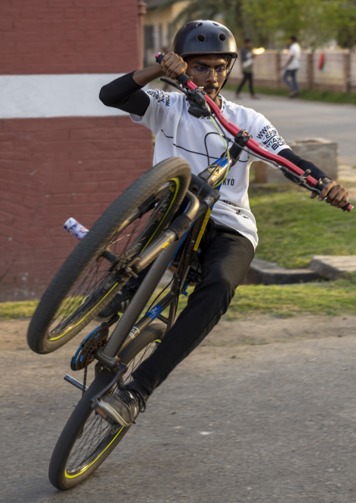 Young bangladeshi male BMX rider performing wheelie in urban area, Khulna Division, Jessore, Bangladesh