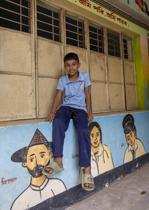 Bangladeshi boy sit on a school mural depicting ethnies, Dhaka Division, Delduar, Bangladesh