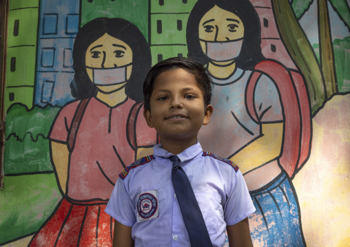 Boy in front of a school mural depiciting pupils with covid masks, Dhaka Division, Rupganj, Bangladesh