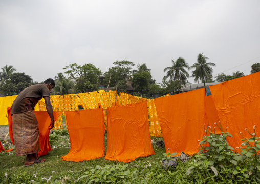 Bangladeshi worker hanging orange fabrics under the sun, Dhaka Division, Rupganj, Bangladesh