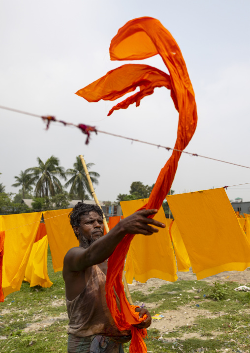 Bangladeshi worker hanging orange fabrics under the sun, Dhaka Division, Rupganj, Bangladesh