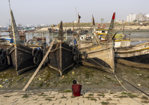 Bangladeshi man sit in front of trawlers in the fish market, Chittagong Division, Chittagong, Bangladesh