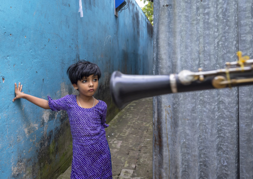 Bangladeshi girl in the street looking at a musician playing trumpet, Dhaka Division, Munshiganj Sadar, Bangladesh