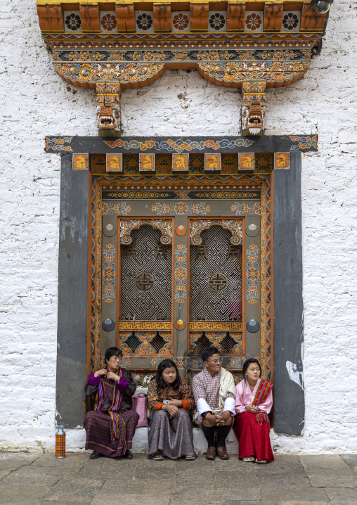 Bhutanese family sit in front of a door in Nyenzer Lhakhang, Punakha dzongkhag, Punakha, Bhutan
