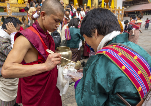 Monk giving black lentils with milk to pilgrims in Punakha dzong, Punakha dzongkhag, Punakha, Bhutan