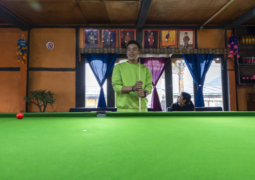 Bhutanese man with King portraits behind him playing snooker, Chhoekhor Gewog, Bumthang, Bhutan