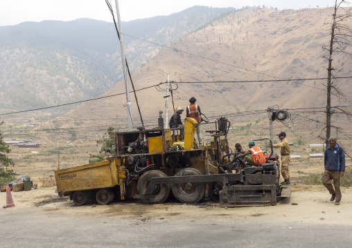 Indian workers placing new coating of asphalt on the road, Wangchang Gewog, Paro, Bhutan