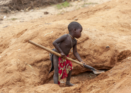 Mucubal tribe boy digging with a shovel to find water, Namibe Province, Virei, Angola