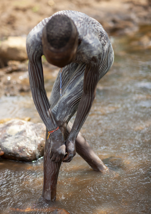 Suri man painting his body with clay in a river, Turgit, Omo valley, Ethiopia