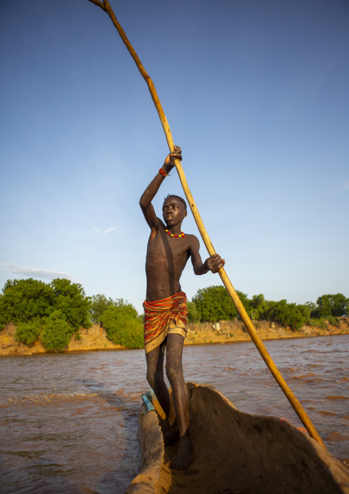 Young boy pushing a boat on the omo river, Omorate, Omo valley, Ethiopia