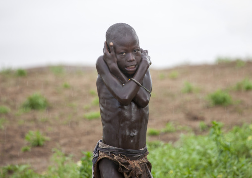 Kid from Karo tribe freezing under the rain, Korcho, Omo valley, Ethiopia