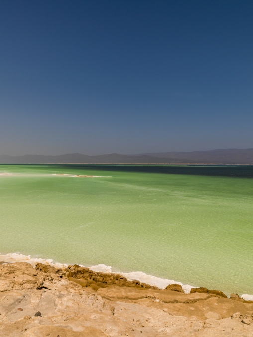 Vivid turquoise water stretches toward a hazy distant mountain range, Dikhil Region, Lake Assal, Djibouti