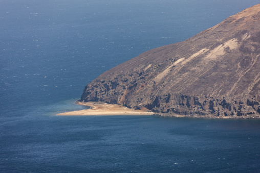 Steep volcanic cliffs descend to a small sandy beach at the Devil's Cauldron, Tadjourah Region, Goubet Al-kharab, Djibouti