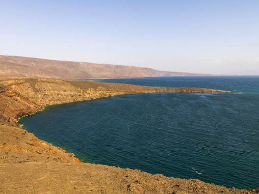 Dark volcanic headlands frame a deep blue bay beneath distant cliffs, Tadjourah Region, Goubet Al-kharab, Djibouti