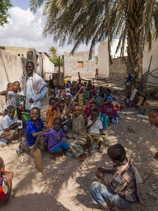 Afar children sit under a palm tree holding wooden boards in an outdoor Quranic school, Tadjourah Region, Tadjoura, Djibouti