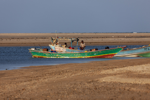 A colorful wooden fishing boat carries three men near the shore, Obock Region, Gorodia, Djibouti
