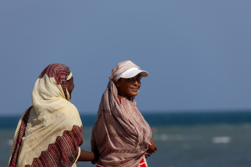 Two women in headscarves walk together by the sea, Obock Region, Obock, Djibouti