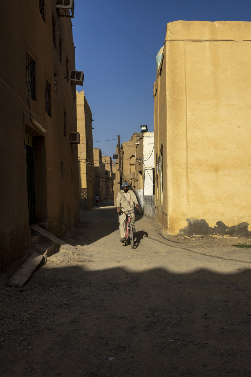 Man riding a bicycle through a narrow alley between tall mudbrick houses, Ad Dakhiliyah Region, Al Hamra, Oman