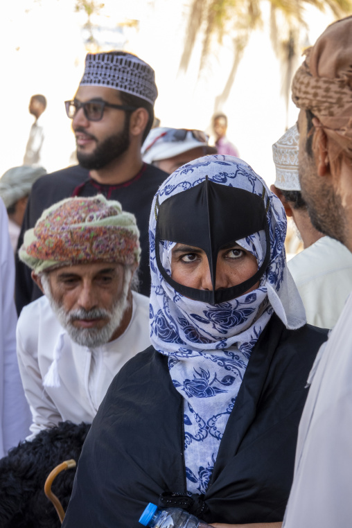 Group of Omani people including a woman wearing a traditional black burqa face mask gathered at the livestock market, Ad Dakhiliyah Region, Nizwa, Oman
