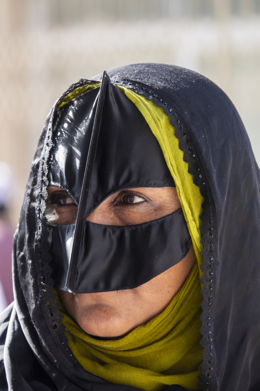 Close-up portrait of a woman wearing a lace-trimmed black traditional burqa face mask and an olive green headscarf, Ad Dakhiliyah Region, Nizwa, Oman