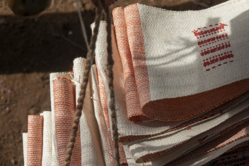 Folded Senufo cotton cloths with orange stripes and embroidered patterns catch the sunlight at a street market, Savanes district, Waraniene, Ivory Coast