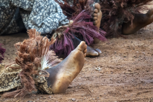 Bare feet emerge from raffia masquerade costumes worn by African musicians lying on the ground, Savanes district, Waraniene, Ivory Coast