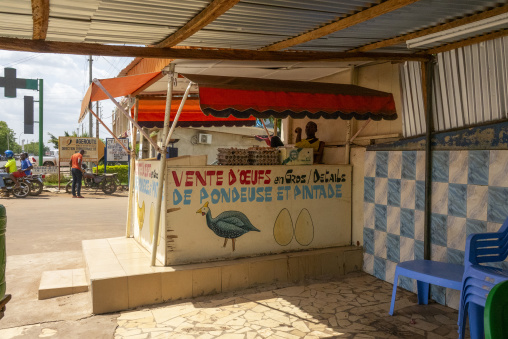 A roadside stall sells eggs and guinea fowl beneath a painted sign, Poro region, Korhogo, Ivory Coast