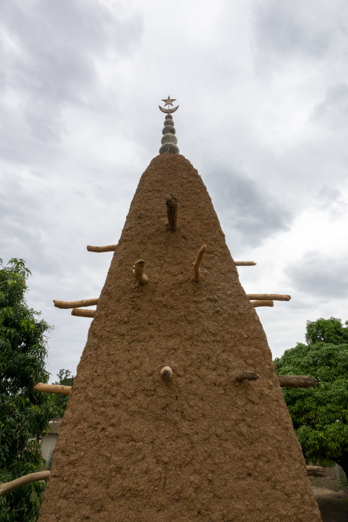 Three bell-shaped ceramic caps top pinnacles framed by lush mango foliage at the 17th-century Sudano-Sahelian mosque, Savanes district, Kouto, Ivory Coast