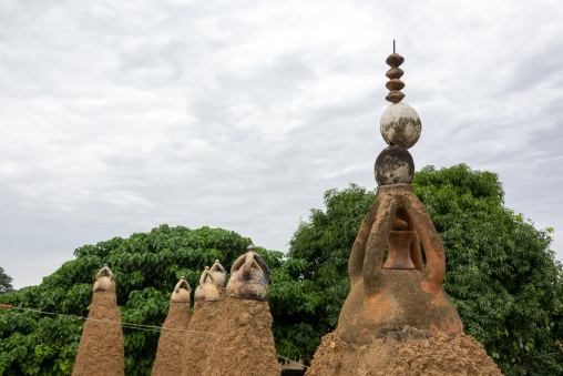 Ceramic-capped pinnacles cluster beneath a crescent finial half-hidden by leaves at the 17th-century Sudano-Sahelian mosque, Savanes district, Kouto, Ivory Coast
