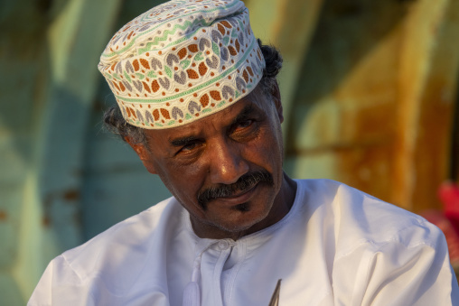 Portrait of a mustached man wearing a white embroidered Omani cap and white dishdasha looking at the camera, Dhofar Governorate, Mirbat, Oman