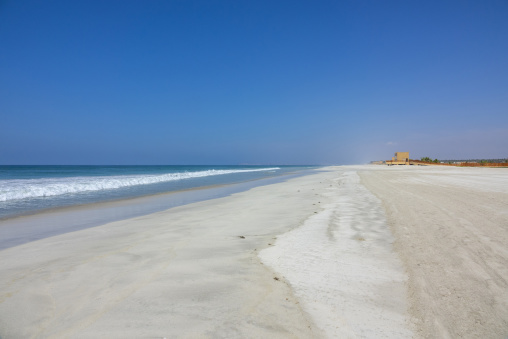 Wide sandy beach with breaking waves and a beachfront building in the distance, Dhofar Governorate, Salalah, Oman