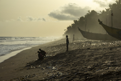 Children play together on a littered beach near fishing boats in N'zima village, Sud-Comoé, Grand-Bassam, Ivory Coast