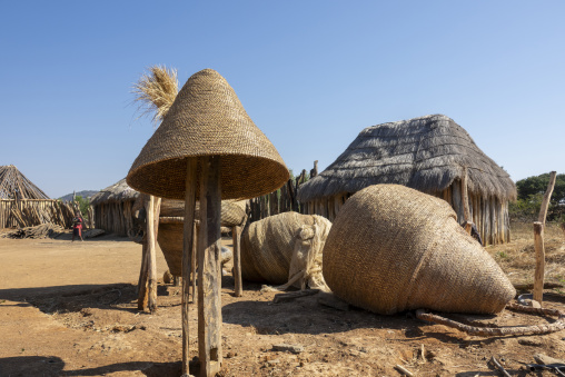 Woven grain silos standing in front of thatched huts in a Mwila village, Huila Province, Chibia, Angola