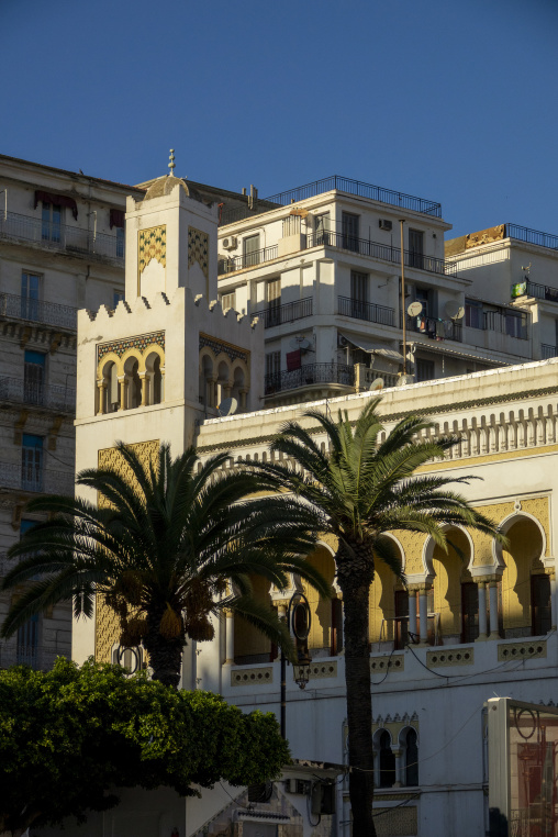 Moorish-style building with a crenellated tower framed by palm trees amid modern apartment blocks, North Africa, Algiers, Algeria