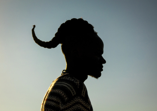 Silhouette of a man with a curved forward-curling hairstyle against the sky at sunset, Cunene Province, Oncocua, Angola