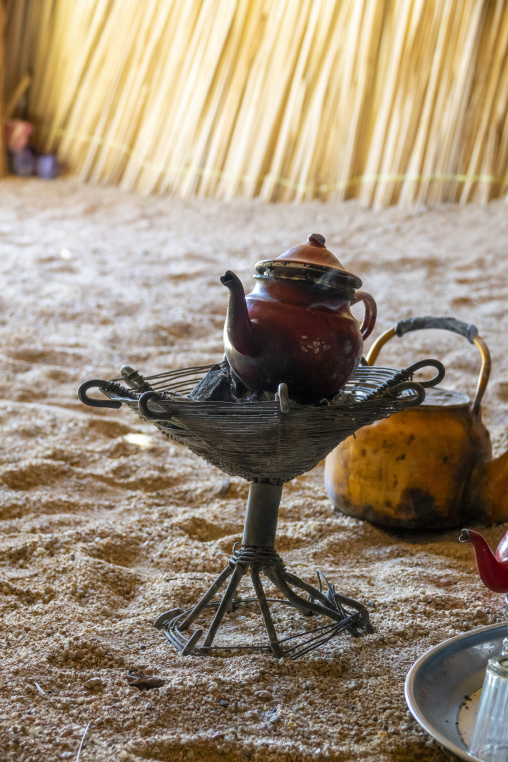 Traditional Tuareg teapot brewing on a woven charcoal stand inside a desert tent, North Africa, Tamanrasset, Algeria