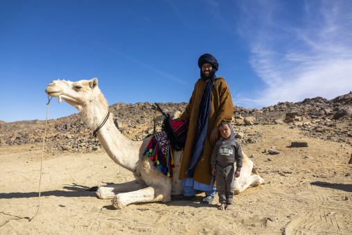 Close-up of a camel's head with a Tuareg man and child standing nearby in the desert, North Africa, Tamanrasset, Algeria