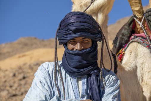 Portrait of a Tuareg man wearing an indigo tagelmust turban beside his camel, North Africa, Tamanrasset, Algeria