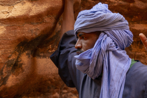 Tuareg guide in a blue turban examining ancient rock art on a canyon wall, Tassili N'Ajjer National Park, Tadrart Rouge, Algeria