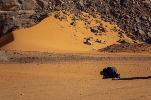 Tuareg man kneeling in prayer on a sand dune in the desert, Tassili N'Ajjer National Park, Tadrart Rouge, Algeria